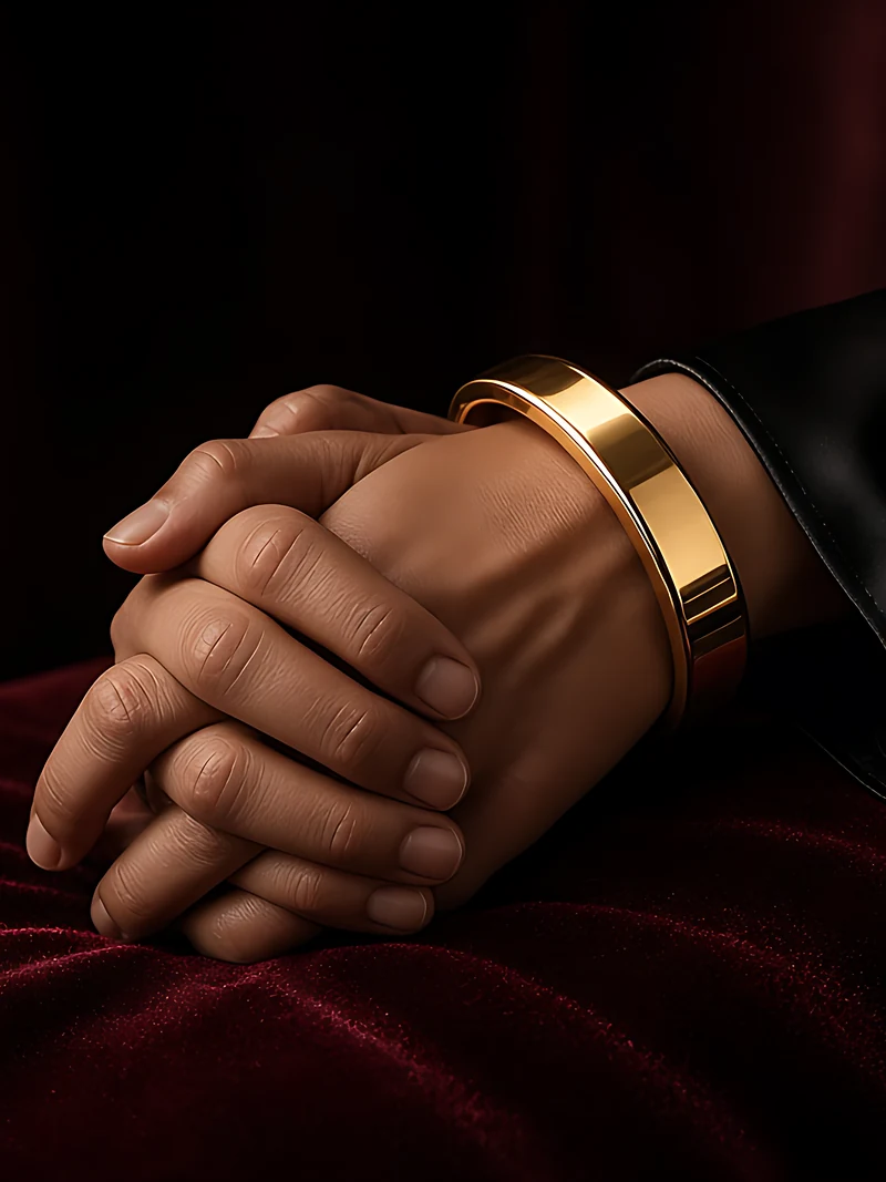 Clasped hands resting on burgundy velvet, one wrist wearing a wide polished gold bangle