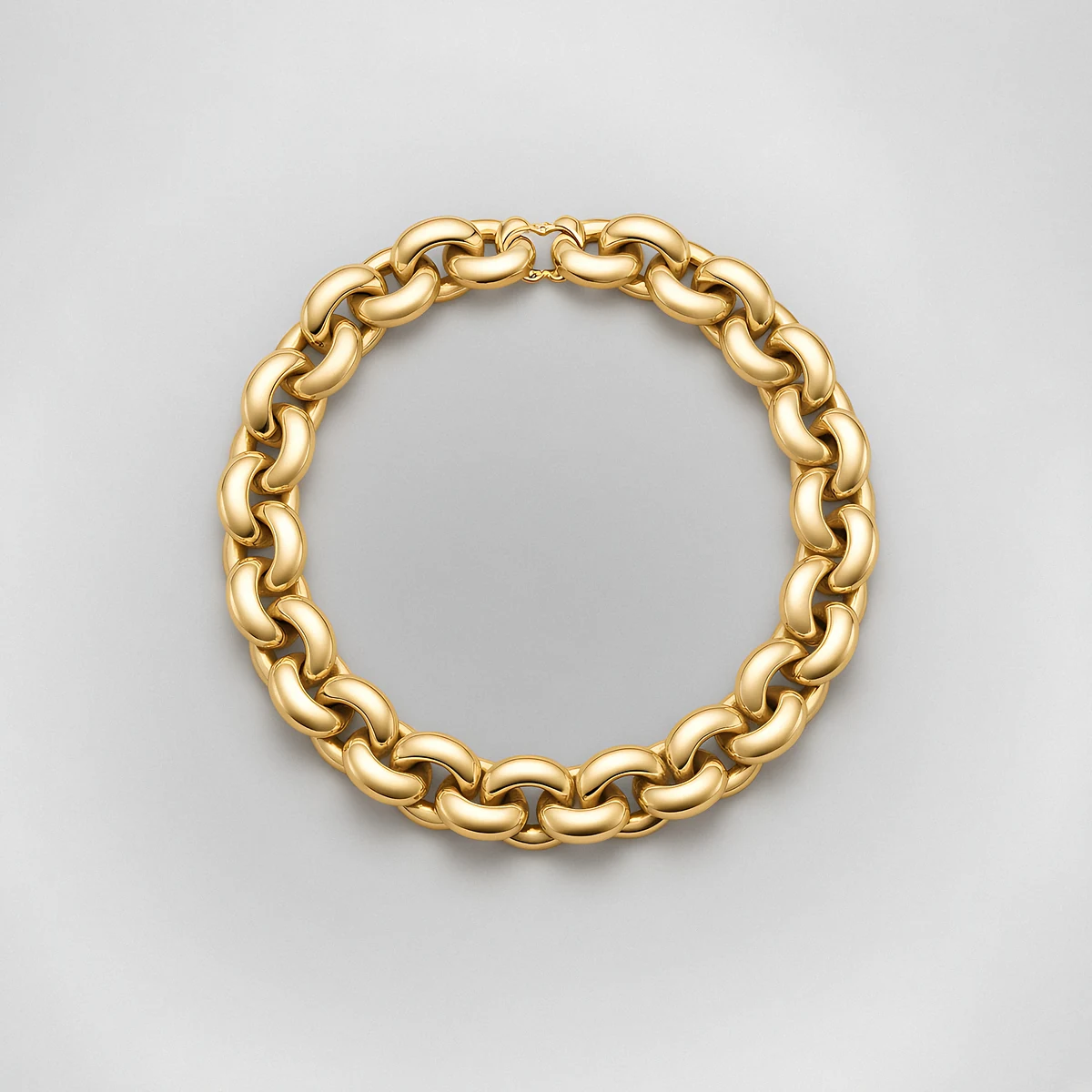 A chunky polished gold link collar necklace on a pale grey background