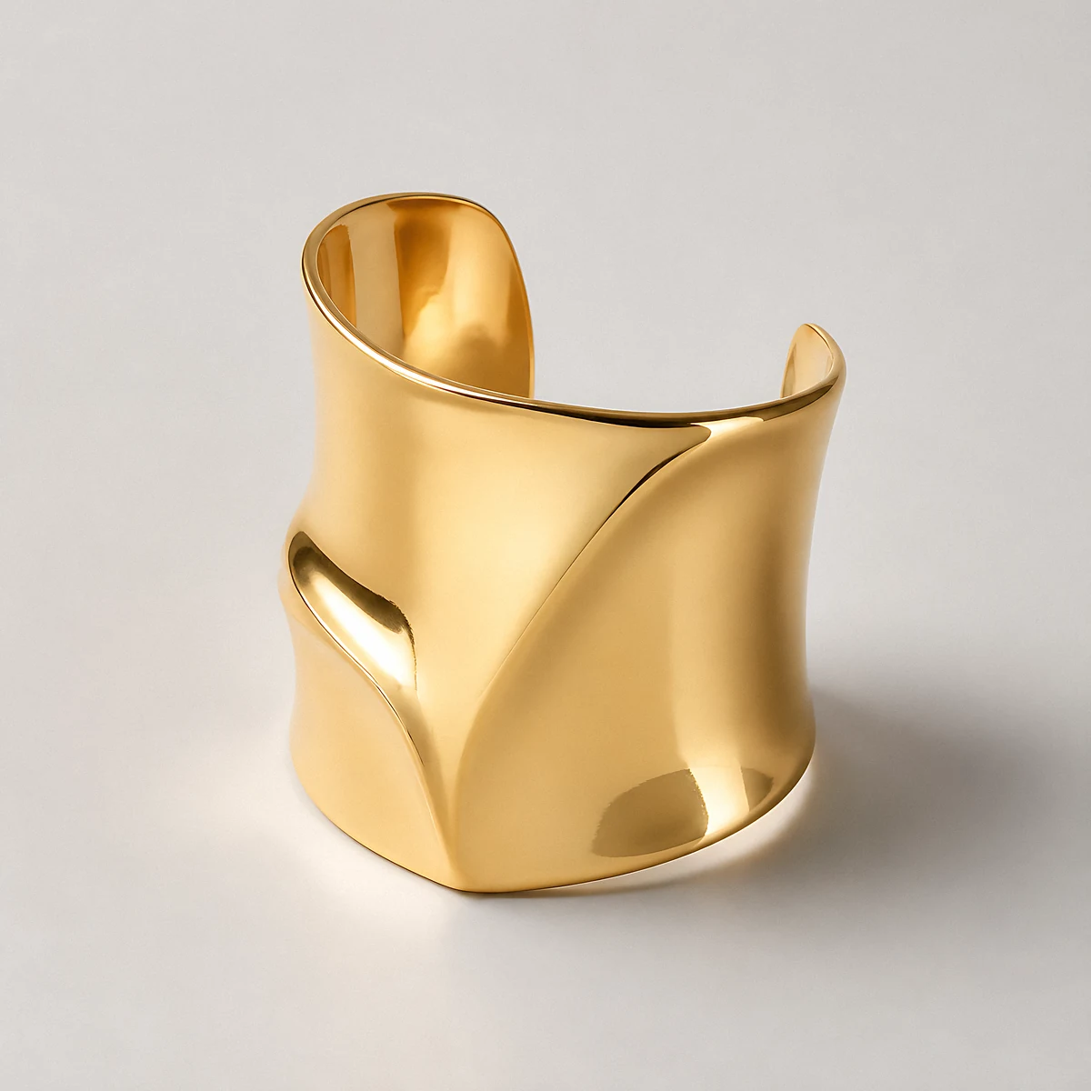 A wide sculptural gold cuff bracelet photographed in the studio