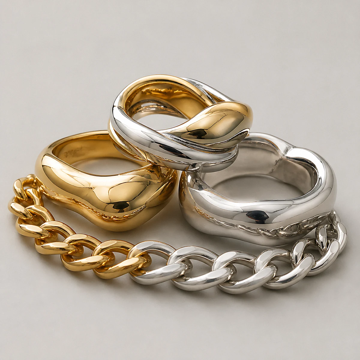 Gold, silver and two-tone chunky rings beside a two-tone curb chain photographed in the studio