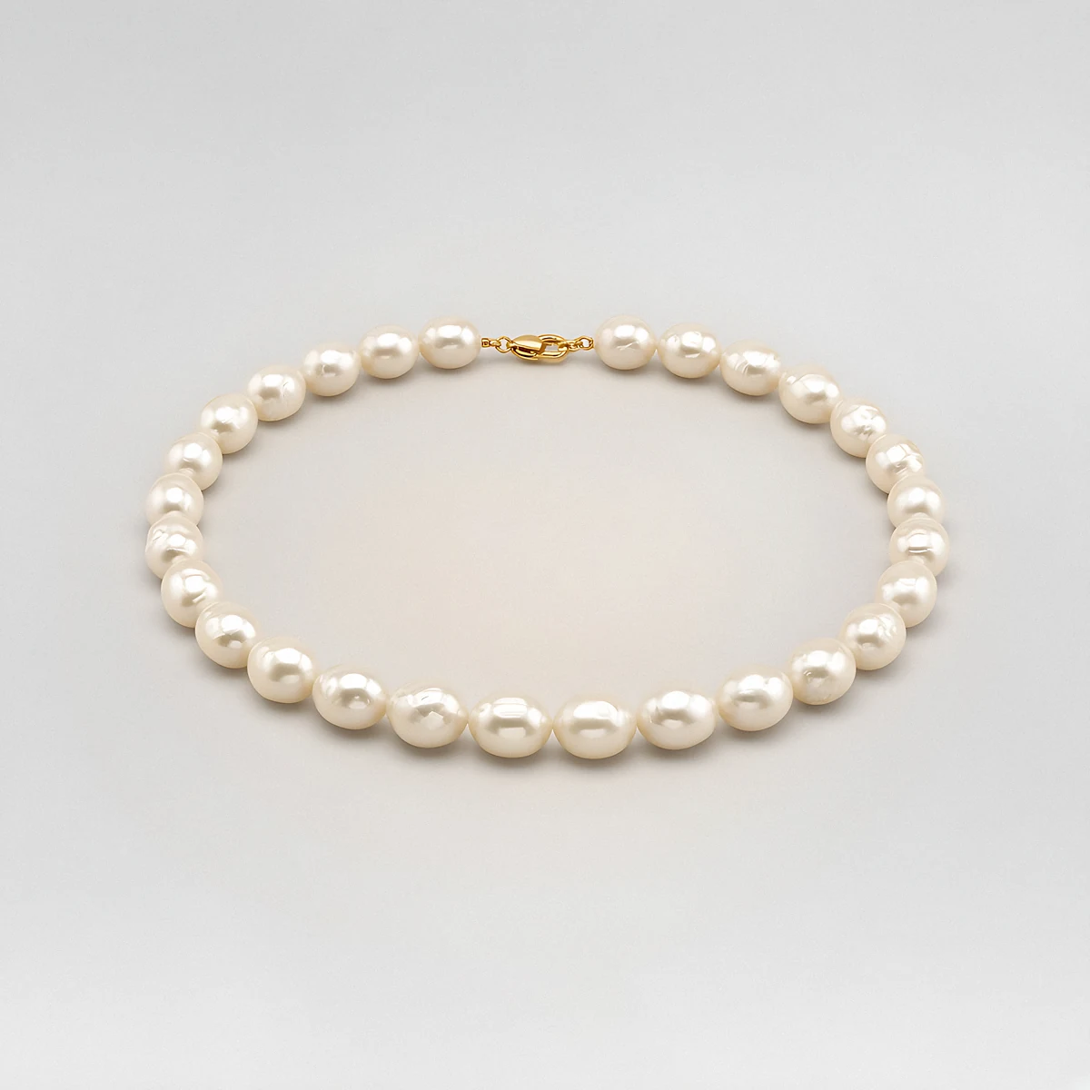 A strand of large cream baroque pearls with a gold clasp on a pale grey background