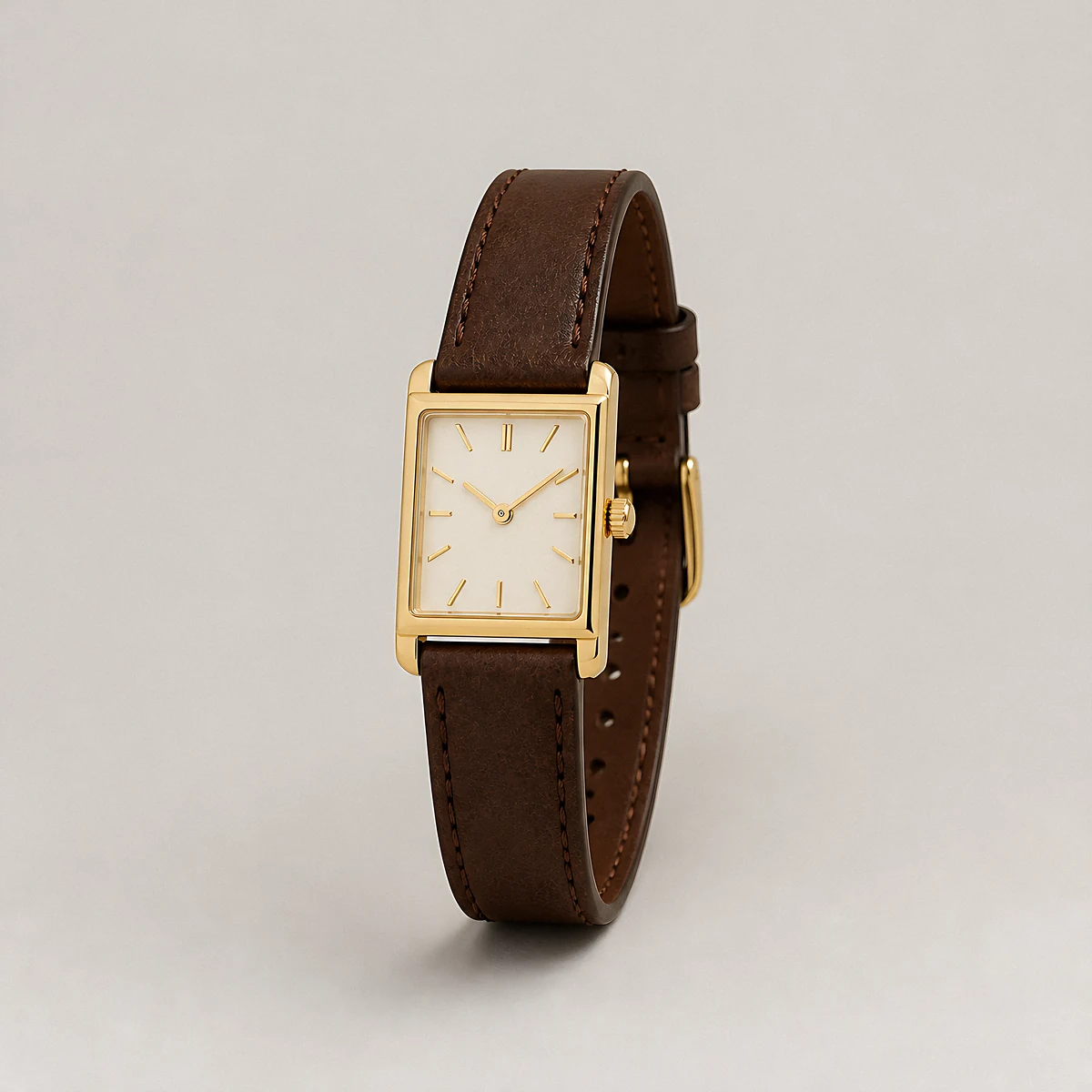 A tiny rectangular gold watch on a brown leather strap photographed in the studio