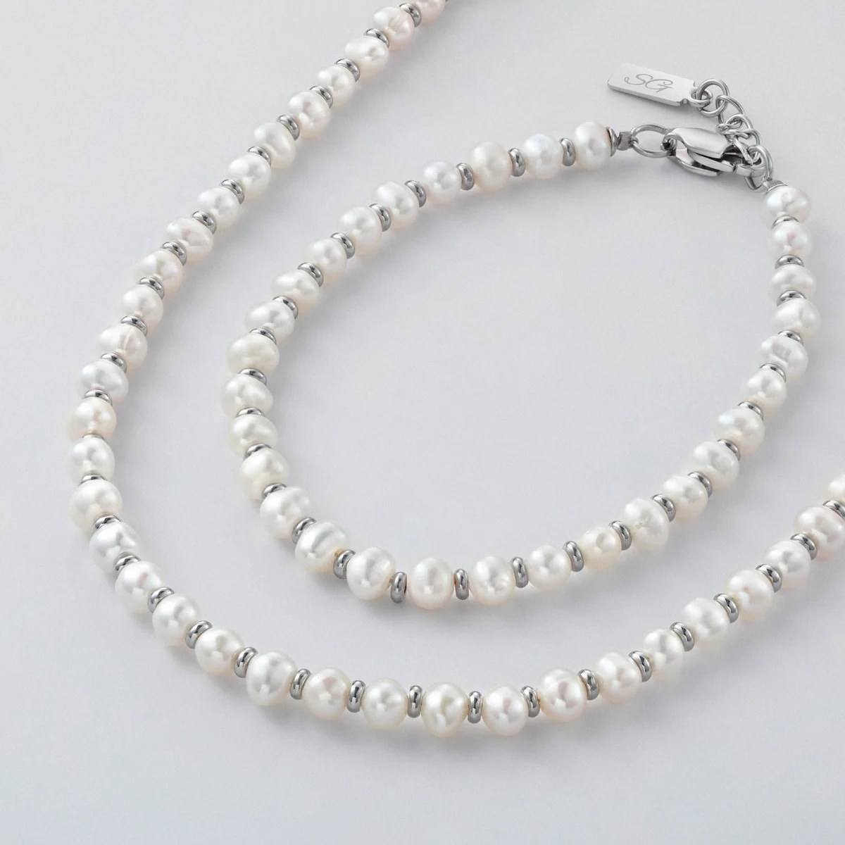 A strand of small white freshwater pearls spaced with silver beads beside a matching pearl bracelet